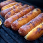 Golden-brown burnt hotdogs pieces smothered in tangy barbecue sauce, served on mini slider buns with melted cheese and fresh cilantro